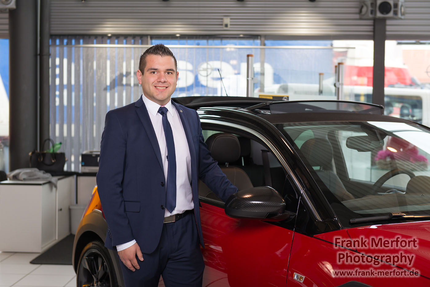 Geschäftsmann steht neben einem Auto in einem Autohaus